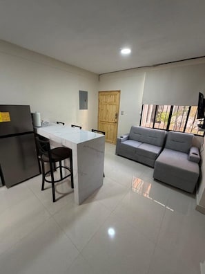 Una cocina compacta con una isla central, un sofá gris y una puerta de madera.