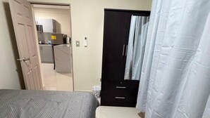 Een slaapkamer met een bed, een kledingkast, een badkamer met douchegordijn en een kitchenette op de achtergrond.