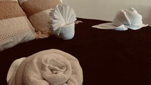A neatly made bed with a rolled towel in the foreground, a pillow with a textured pattern, and a small white container on the bed. - Pelicanos  (Alvarado)