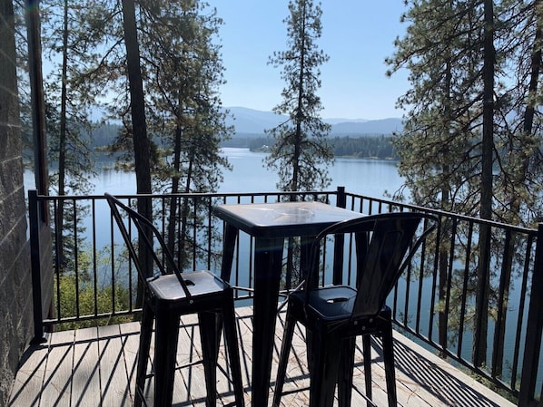A deck with a table and chairs overlooking a lake, surrounded by trees and mountains.