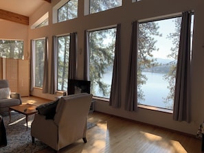 A spacious living room with large windows, a sofa, a TV, and a view of a lake.