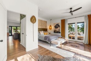Un dormitorio con cama, una banca, ventilador de techo y vistas a través de un ventanal.