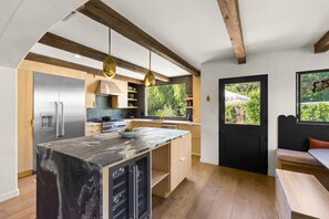Una cocina moderna con una isla de mármol, electrodomésticos de acero inoxidable, vigas de madera y vistas a zonas verdes.