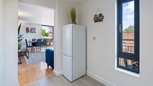 Eine kleine Küche mit Kühlschrank, eine Essecke mit Stühlen und Tisch sowie ein Blick durch ein Fenster.