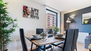 Ein Essbereich mit einem Tisch für vier Personen, Stühlen, einem Blumentopf und Blick auf die Stadtlandschaft durch das Fenster.