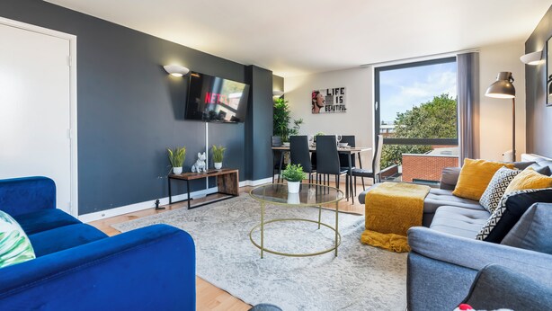 Ein modernes Wohnzimmer mit Sofa, Couchtisch, Fernseher und einem Essbereich mit Stühlen und Tisch.