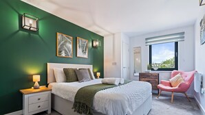 Ein Schlafzimmer mit Bett, Nachttischen, einem Sessel, einem Fenster und Wandbildern.