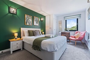 Un dormitorio con cama, mesitas de noche, una silla, una ventana y decoración en la pared.