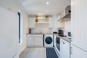 Una cocina moderna con armarios blancos, lavadora integrada y microondas.