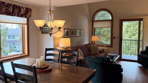 Uma sala de jantar com uma mesa e cadeiras de madeira, um candelabro e vista para uma rua residencial.