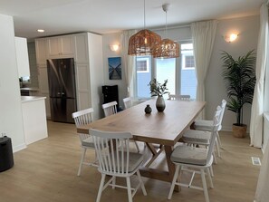 A modern kitchen with white cabinets, a stainless steel refrigerator, and a dining area with a wooden table and white chairs.