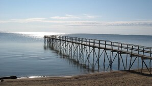 A pier extending into calm water with a sandy beach in the foreground. - Steps from the Shore, Modern Beachy Getaway (Dunnottar)