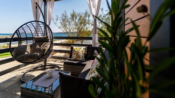 A covered outdoor seating area with a view of the sea, wicker furniture, and a potted plant. - Mobile Home Paradise (Sveti Filip i Jakov)