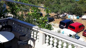 Ein Balkon mit Tisch und Stühlen, der auf eine Küstenlandschaft mit parkenden Fahrzeugen und Grünflächen blickt.