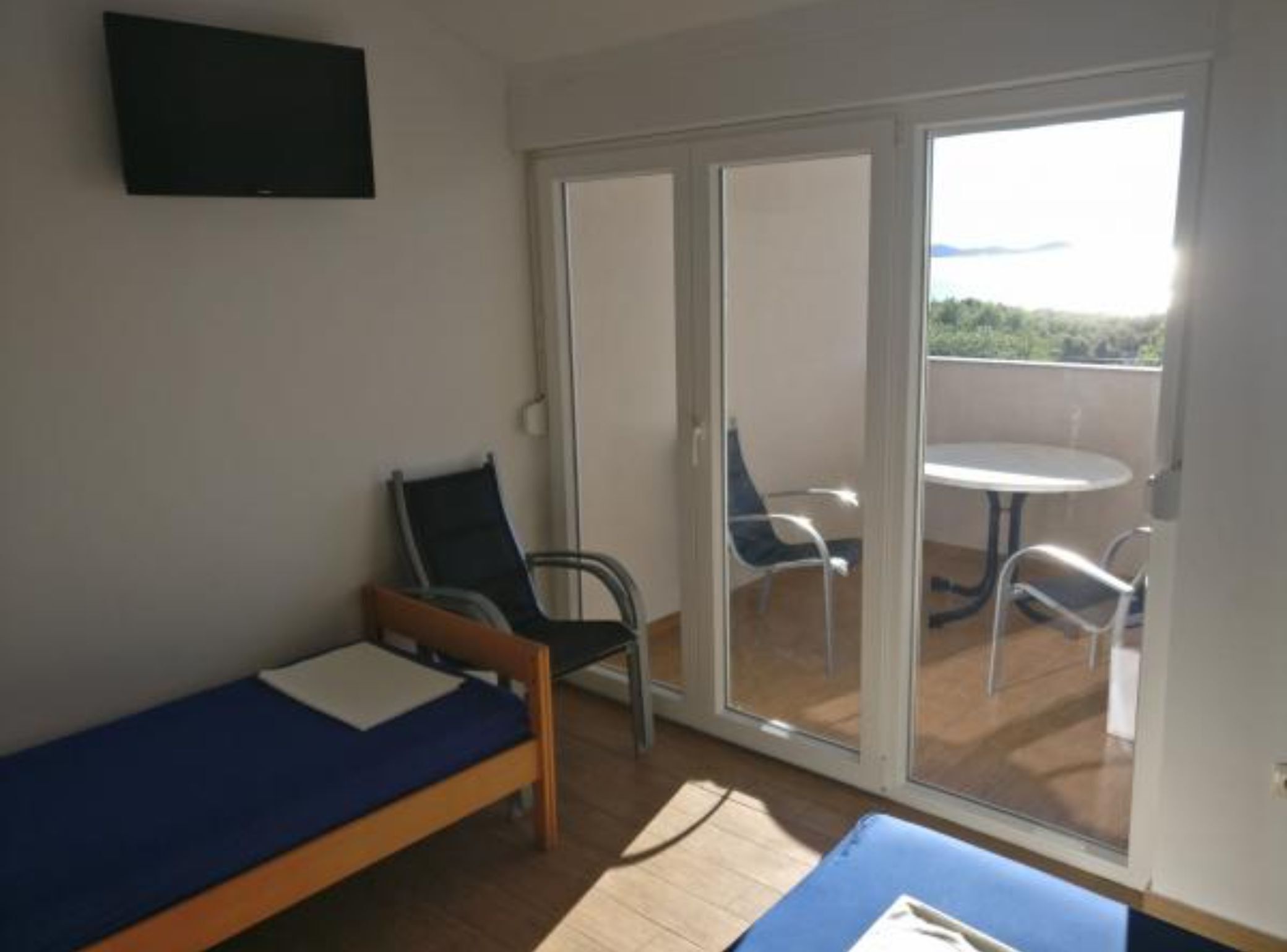 A room with a single bed, a chair, a table, and a sliding glass door leading to an outdoor area with a table and chairs.