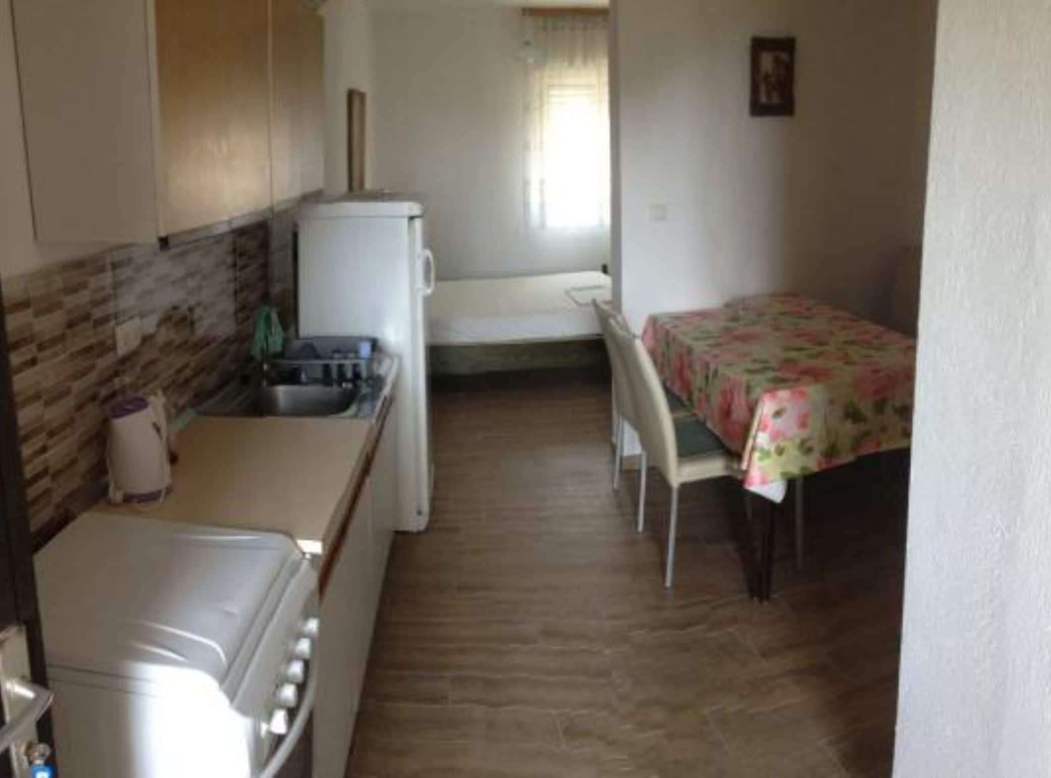 Eine kleine Küchenzeile mit Herd, Spüle und Kühlschrank. Es gibt einen Essbereich mit Tisch und Stühlen.
