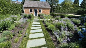 Ein Haus mit einem Steinweg, der zum Eingang führt, umgeben von gepflegten Gärten und Bäumen.