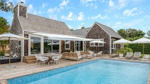 Ein Schwimmbad mit Holzterrasse, Sitzgelegenheiten im Freien und einer überdachten Veranda.