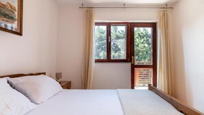 Un dormitorio con cama, mesita de noche, ventana con cortinas y vistas a zonas verdes.