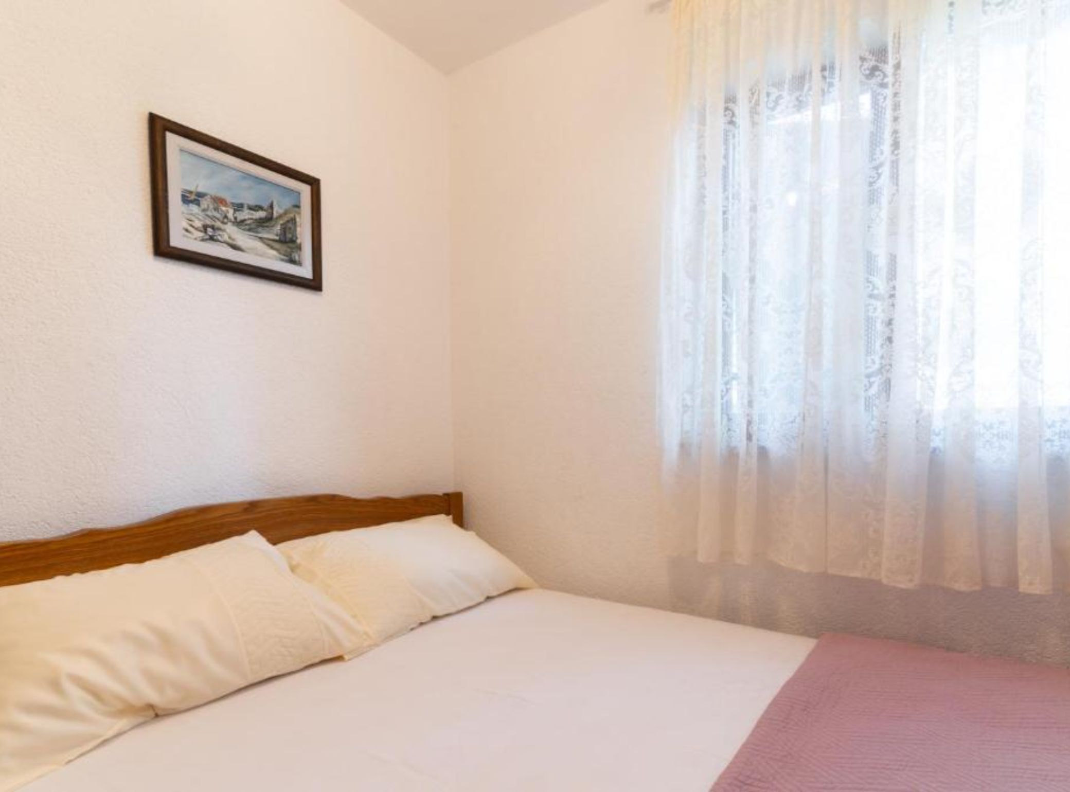 Un dormitorio con cama, un cuadro enmarcado en la pared y cortinas translúcidas.