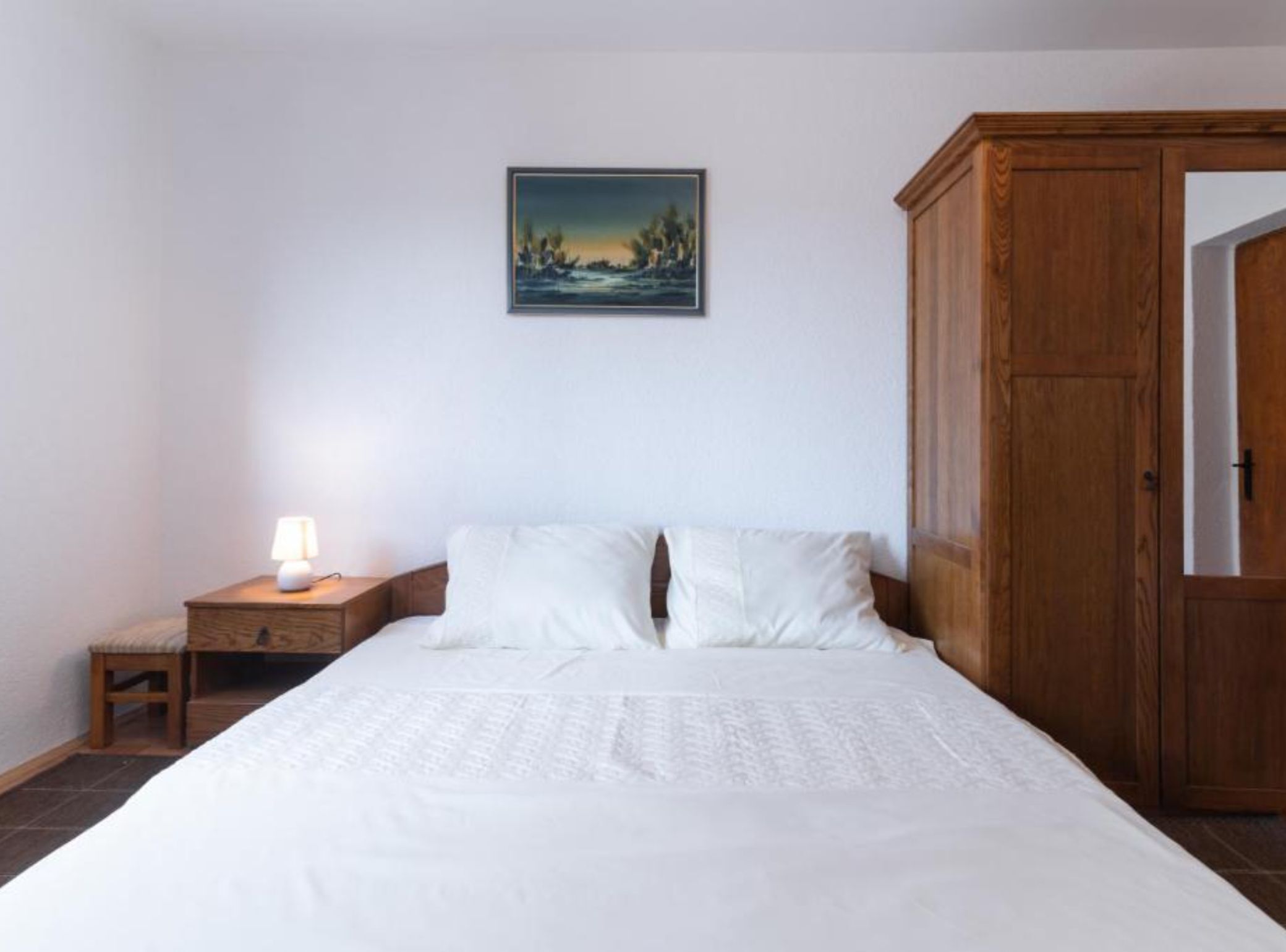 Une chambre à coucher avec un lit, une table de chevet avec une lampe, une armoire en bois et un tableau accroché au mur.