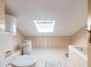Une salle de bain moderne avec un puits de lumière, des toilettes, une baignoire et une douche.