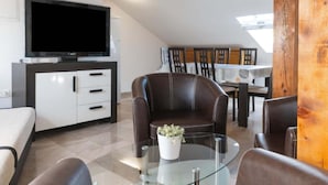 Una sala de estar moderna con televisor de pantalla plana, sillón de cuero, una mesa de centro de vidrio y un comedor con sillas de madera.