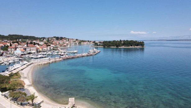 Un pueblo costero con un puerto deportivo, aguas cristalinas y una pequeña isla.