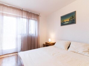 Una camera da letto con un letto, un comodino, una lampada, una finestra con tende e un quadro appeso al muro.