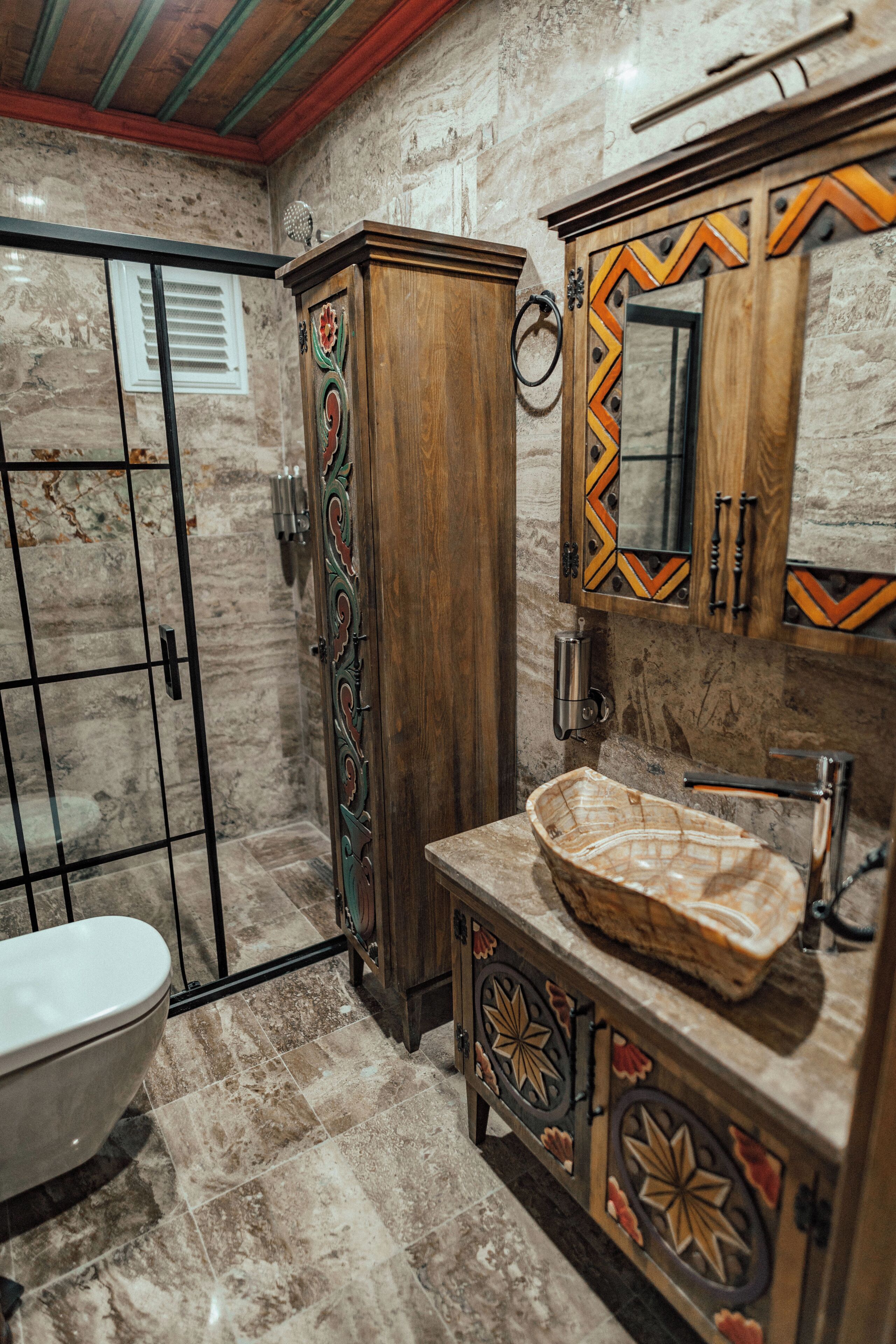 A bathroom with a marble floor, a wooden cabinet, a sink with a decorative basin, and a mirror with a geometric frame.