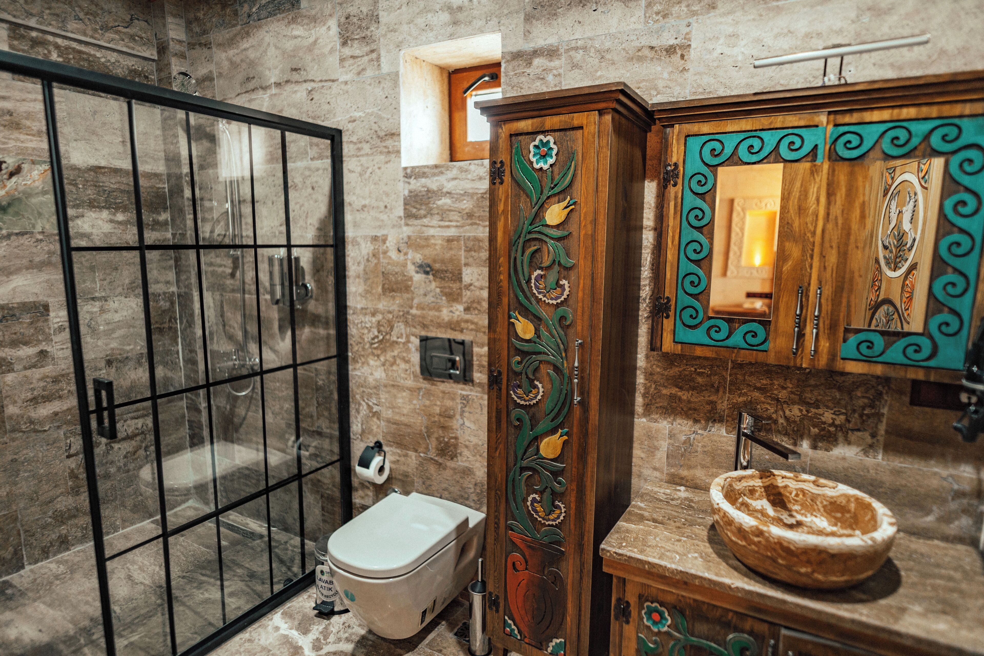 A bathroom with a glass shower enclosure, a toilet, a sink with a decorative basin, and a wooden cabinet with ornate carvings.