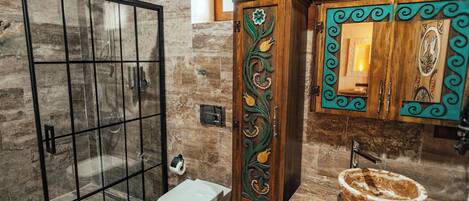 A bathroom with a glass shower enclosure, a toilet, a sink with a decorative basin, and a wooden cabinet with ornate carvings.
