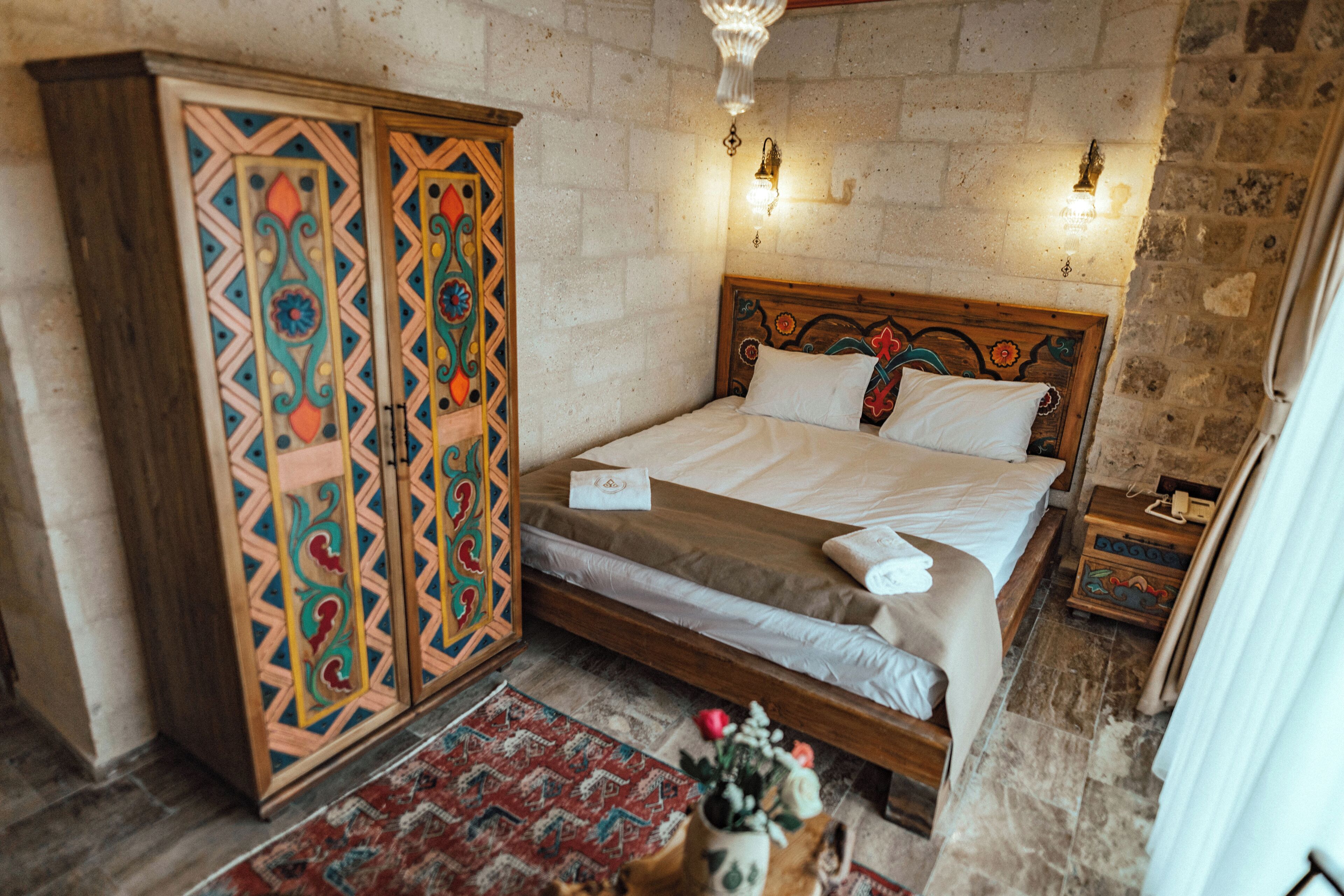 A bedroom with a bed, a wardrobe, a nightstand, and a wall-mounted light fixture.