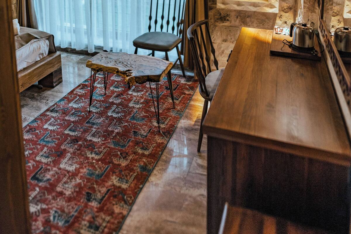 A room with a wooden ceiling, stone walls, a bed, a dining table, chairs, a rug, and a painting.