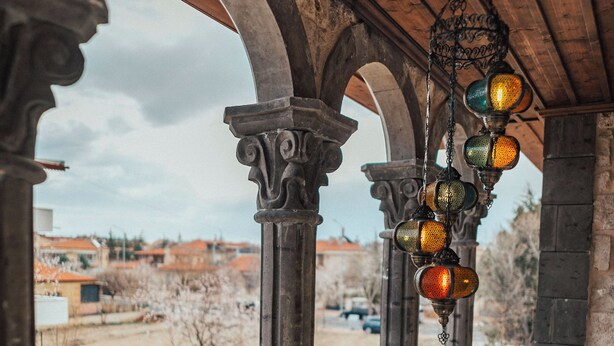 An interior view with arched columns, a hanging light fixture, and a view through a barred window. - Kallista Cappadocia (Nevsehir)