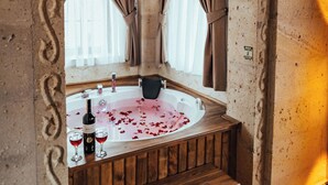 A stone-walled room with a bathtub, wooden bench, and a window with curtains. - Kallista Cappadocia (Nevsehir)