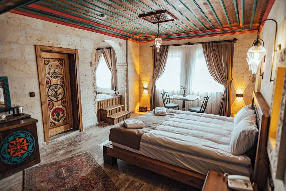 A room with a bed, a wooden bench, a small table, and a chair.