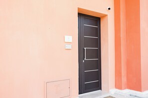 A black door with horizontal handles, a security camera above it, and a small sign on the wall to the left. - Vacation home La Cilinella del.Salento (Copertino)