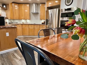 Une cuisine moderne avec des meubles en bois, des appareils en acier inoxydable et un coin repas comprenant une table et des chaises en bois.