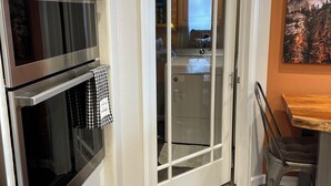 Keittiössä on kaksi uunia, mikroaaltouuni sekä ruokailutila, jossa on puinen pöytä ja metalliset tuolit.