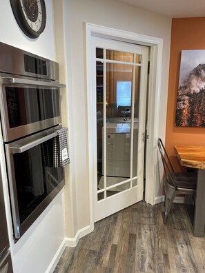 Una cocina con horno doble, microondas y un comedor con mesa de madera y sillas metálicas.