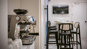 A modern kitchen with a coffee machine, a dining area with chairs and a table, and a flat-screen TV mounted on the wall. - Journeys Kings Cross - Hostel (London)