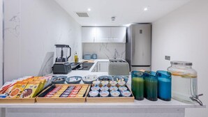 A kitchen with a marble backsplash, a refrigerator, a toaster, and a coffee machine. There are also various food items and containers on the counter. - Journeys Kings Cross - Hostel (London)