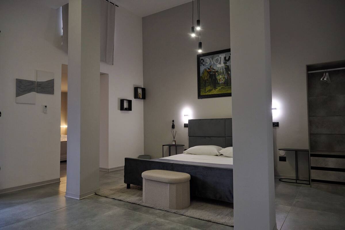 Un dormitorio moderno con una cama grande, mesitas de noche, un banco y obras de arte en las paredes.