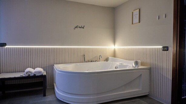 A modern bathroom with a freestanding bathtub, a bench with towels, and a wall-mounted light strip. - Bellosguardo Suites (San Paolo Bel Sito)