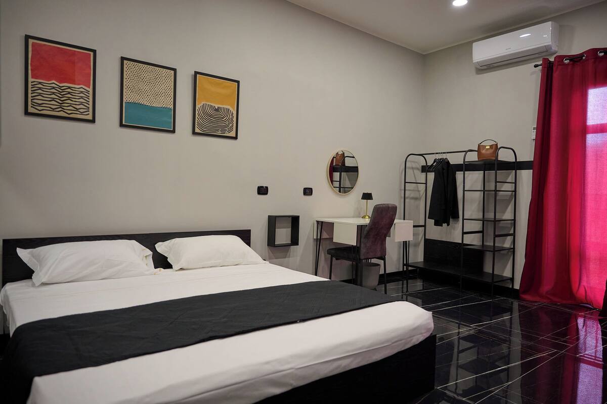 Una habitación de hotel con cama, escritorio, silla, espejo y cortina roja.