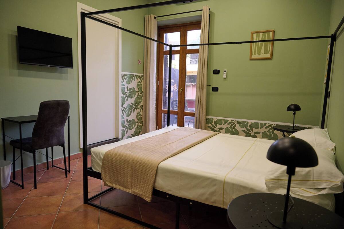 Una cama individual con cabecera, una silla, un escritorio, un televisor y una ventana con cortinas.
