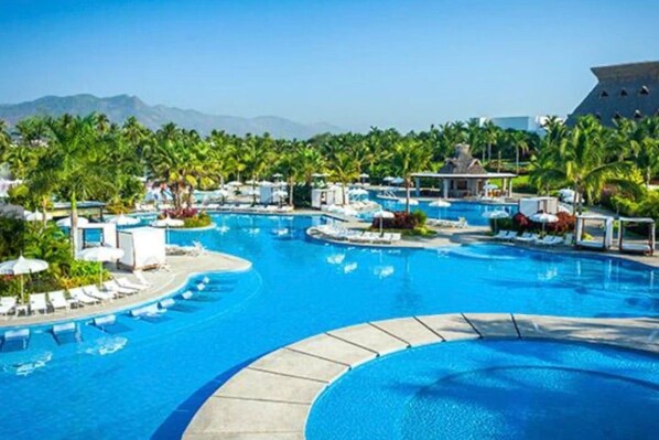A resort pool with multiple sections, palm trees, and lounge chairs.