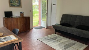 A living room with a sofa, a wooden cabinet, a television, and a door leading outside. - Le Refuge de Crèvecœur (Clef Vallée d'Eure)