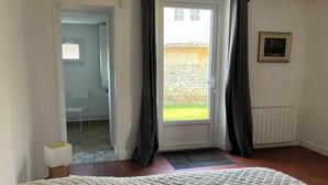 A bedroom with a bed, a door leading to a balcony, a radiator, and a framed picture on the wall. - Le Refuge de Crèvecœur (Clef Vallée d'Eure)